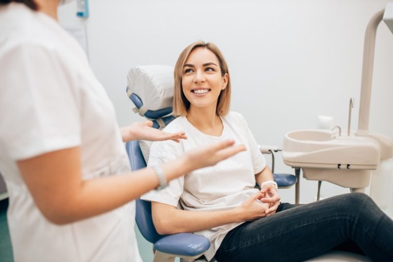 Woman sitting in dentist's chair as a person in scrubs explains something with their hands