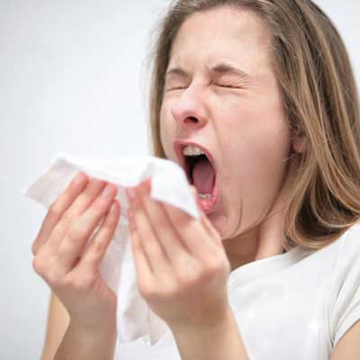 Woman sneezing into a tissue