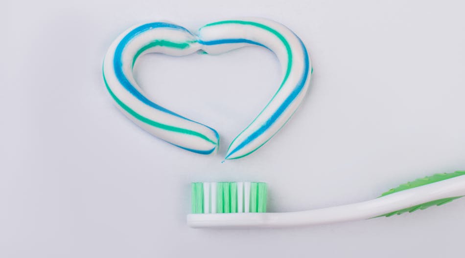 A heart shape drawn with toothpaste sitting above a toothbrush against a pink background